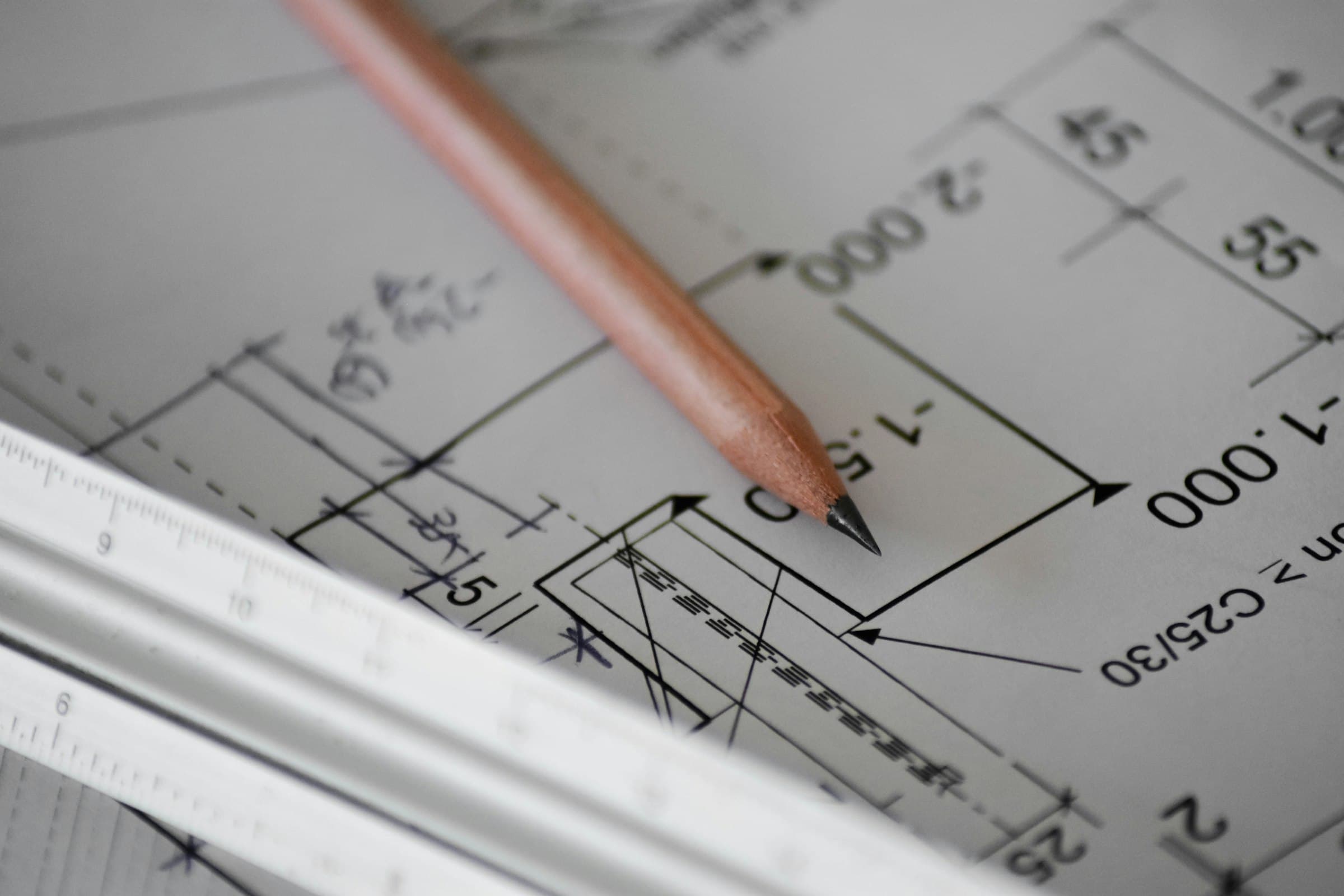 A pencil and scale ruler resting on a dimensioned construction drawing